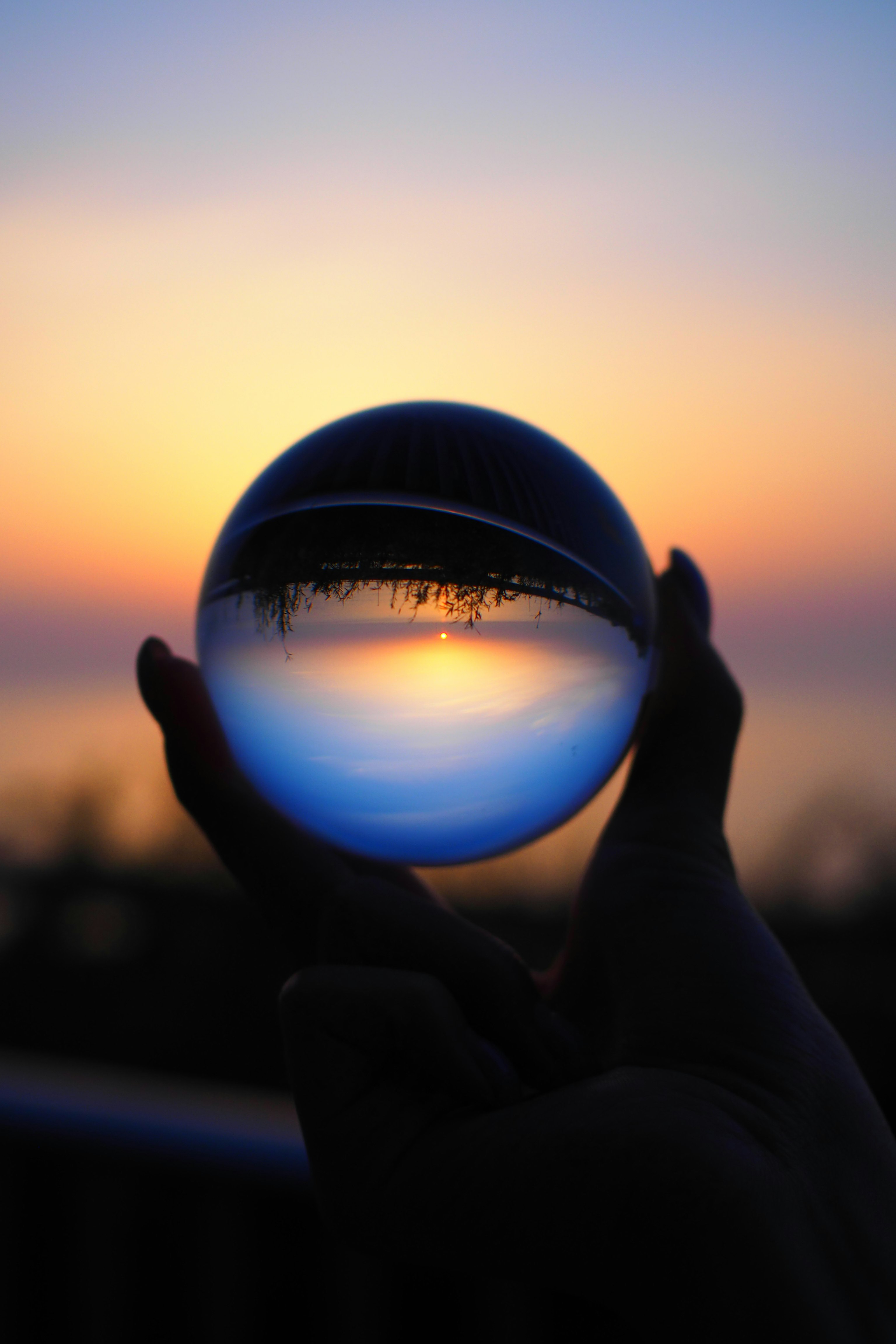 silhouette holding a glass ball reflecting a sunset