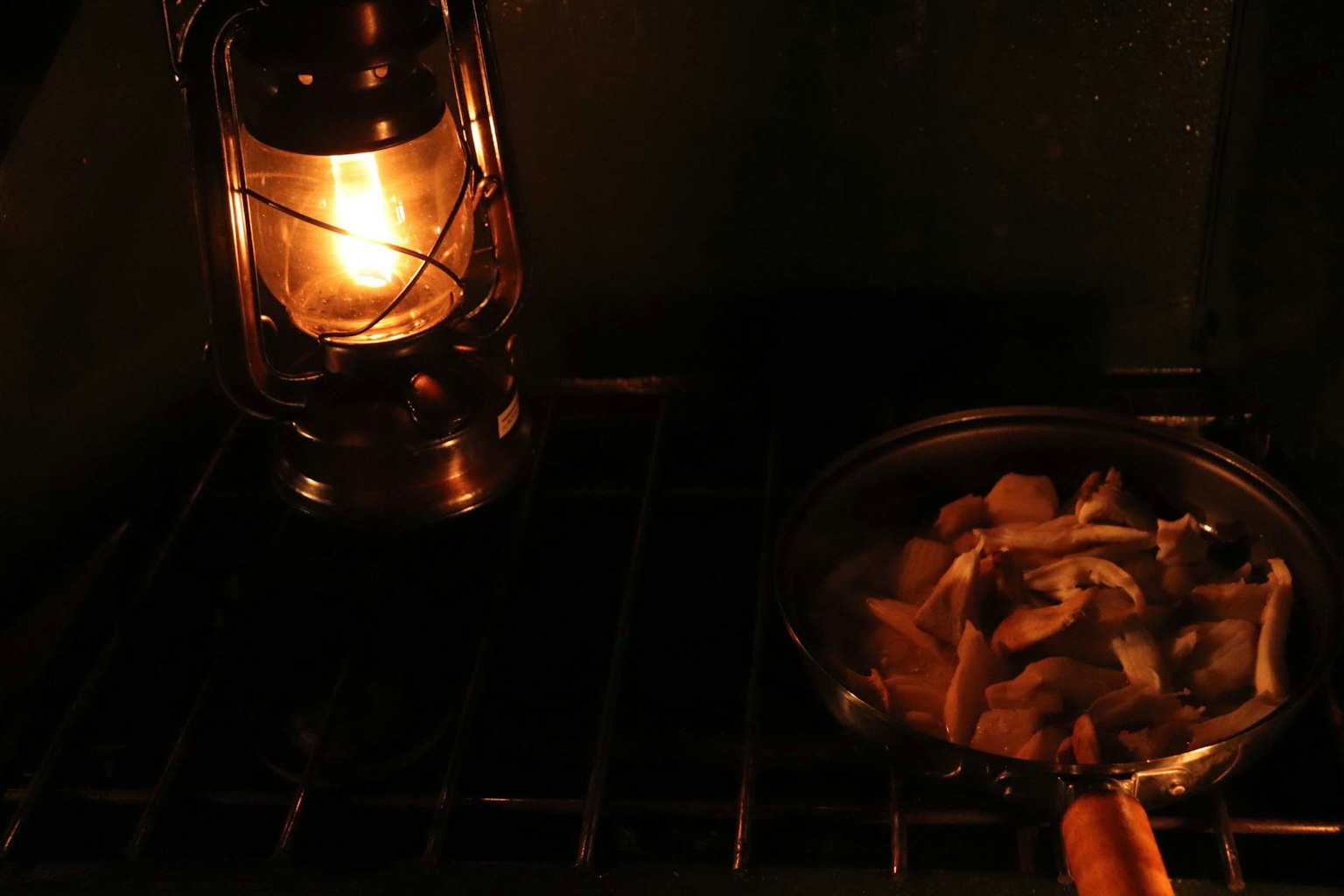 A lantern illuminating a dark space with a pan of food cooking