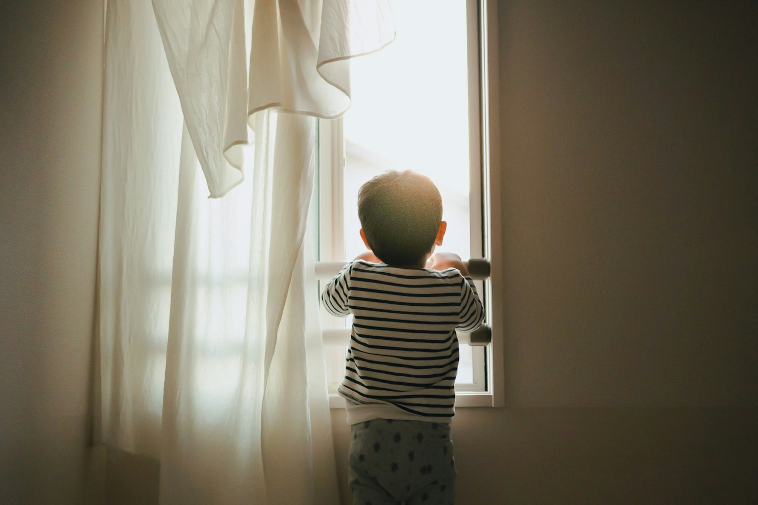 Bóng trẻ em nhìn ra ngoài cửa sổ Rèm mềm với ánh sáng mặt trời chiếu vào
