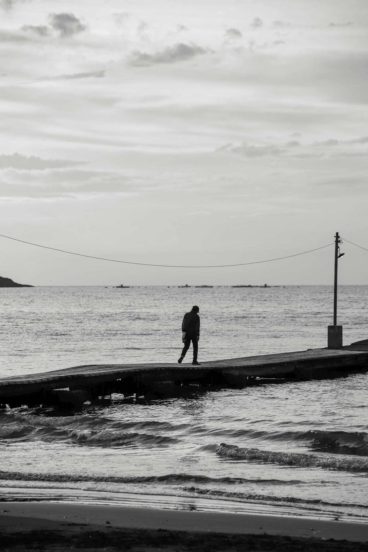 Foto in bianco e nero di una persona in piedi su un molo al mare