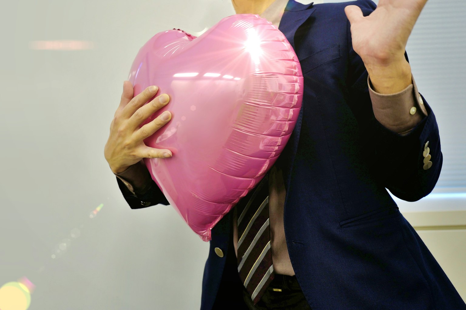 Ein Mann in einem Anzug hält einen großen rosa Herzballon
