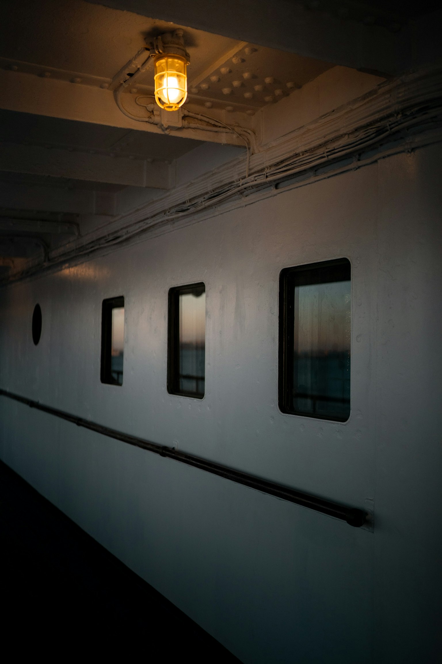 Un couloir de navire avec une lumière suspendue et quatre fenêtres le long du mur blanc