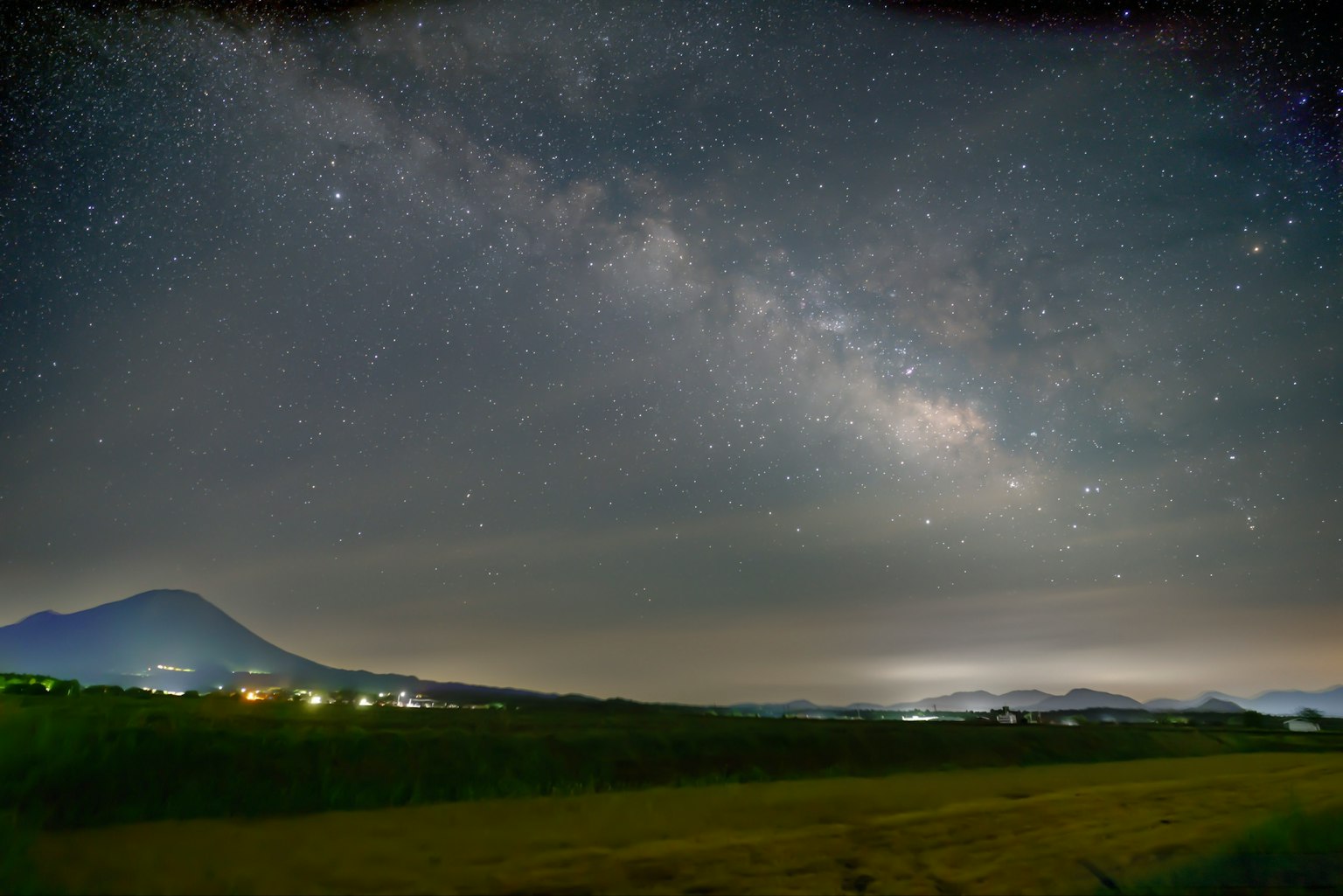 Pemandangan panorama Galaksi Bima Sakti di atas lanskap dengan pegunungan dan lampu jauh