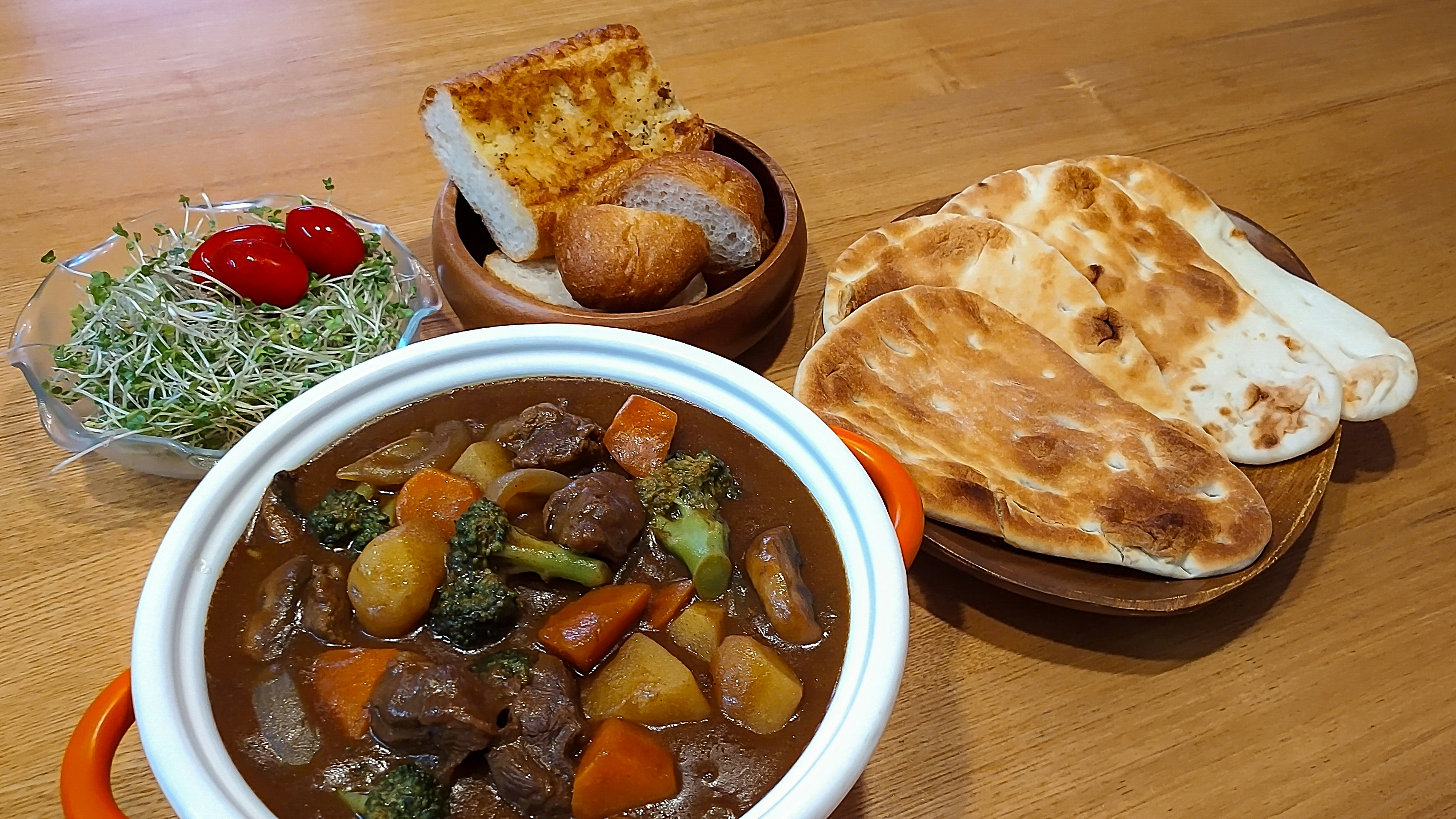 木製テーブルのカレー鍋とナン、サラダ添え