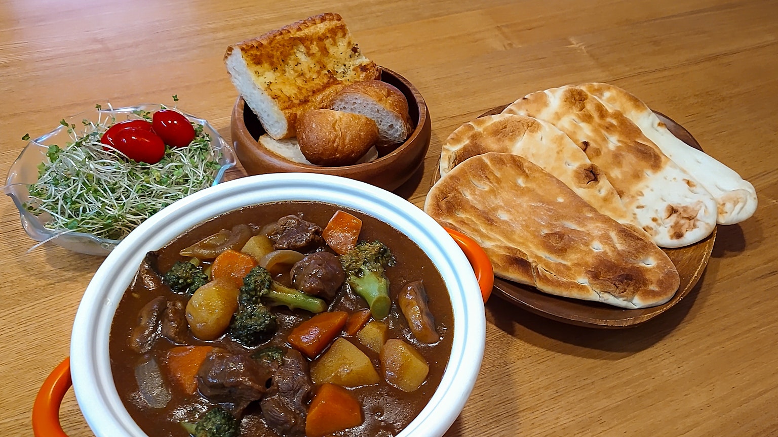 Un delicioso estofado de carne servido con ensalada y varios panes sobre una mesa de madera