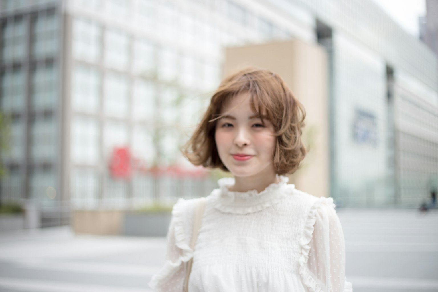 一位穿着白色上衣的年轻女性在城市街道上微笑，背景是现代建筑