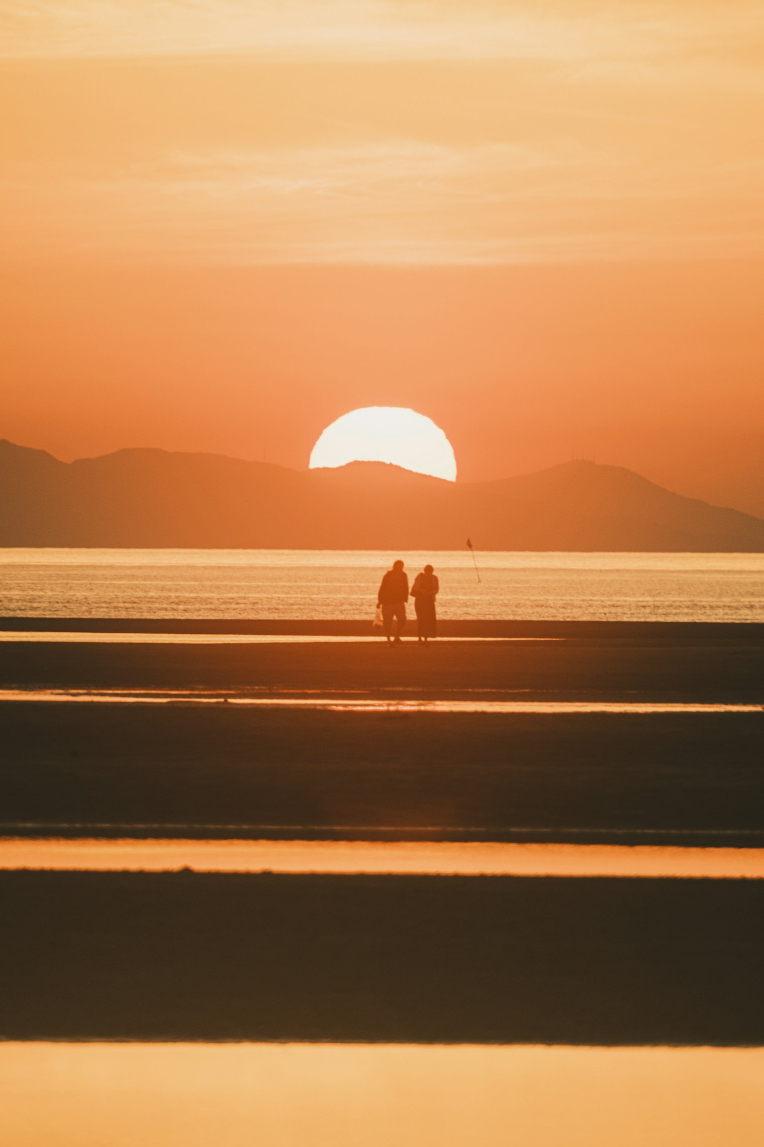 Siluet pasangan yang berjalan di pantai saat matahari terbenam