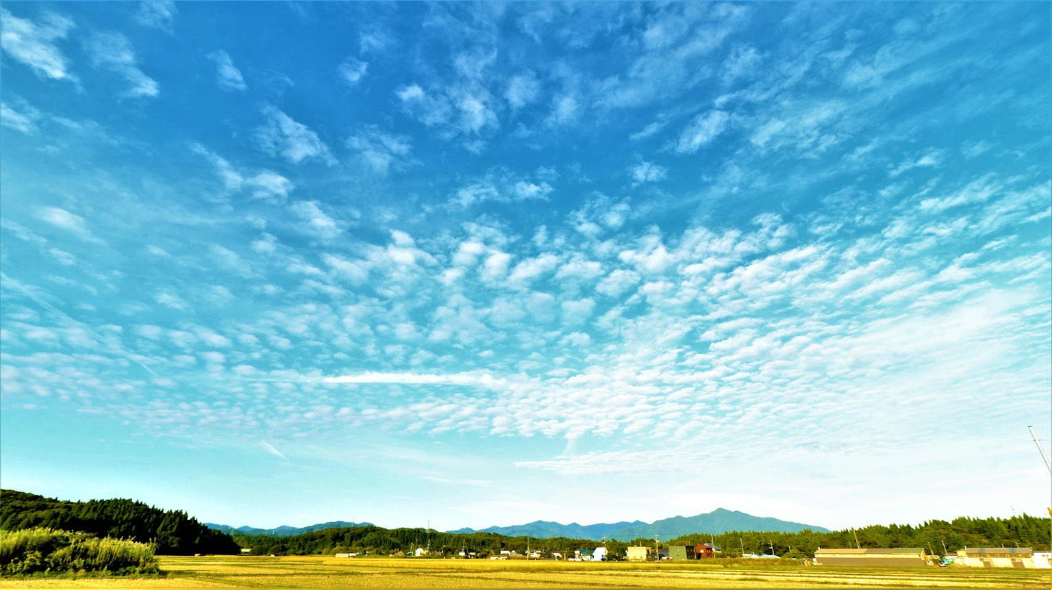 Weitläufiger blauer Himmel mit Wolken Bergen und Feldern im Hintergrund