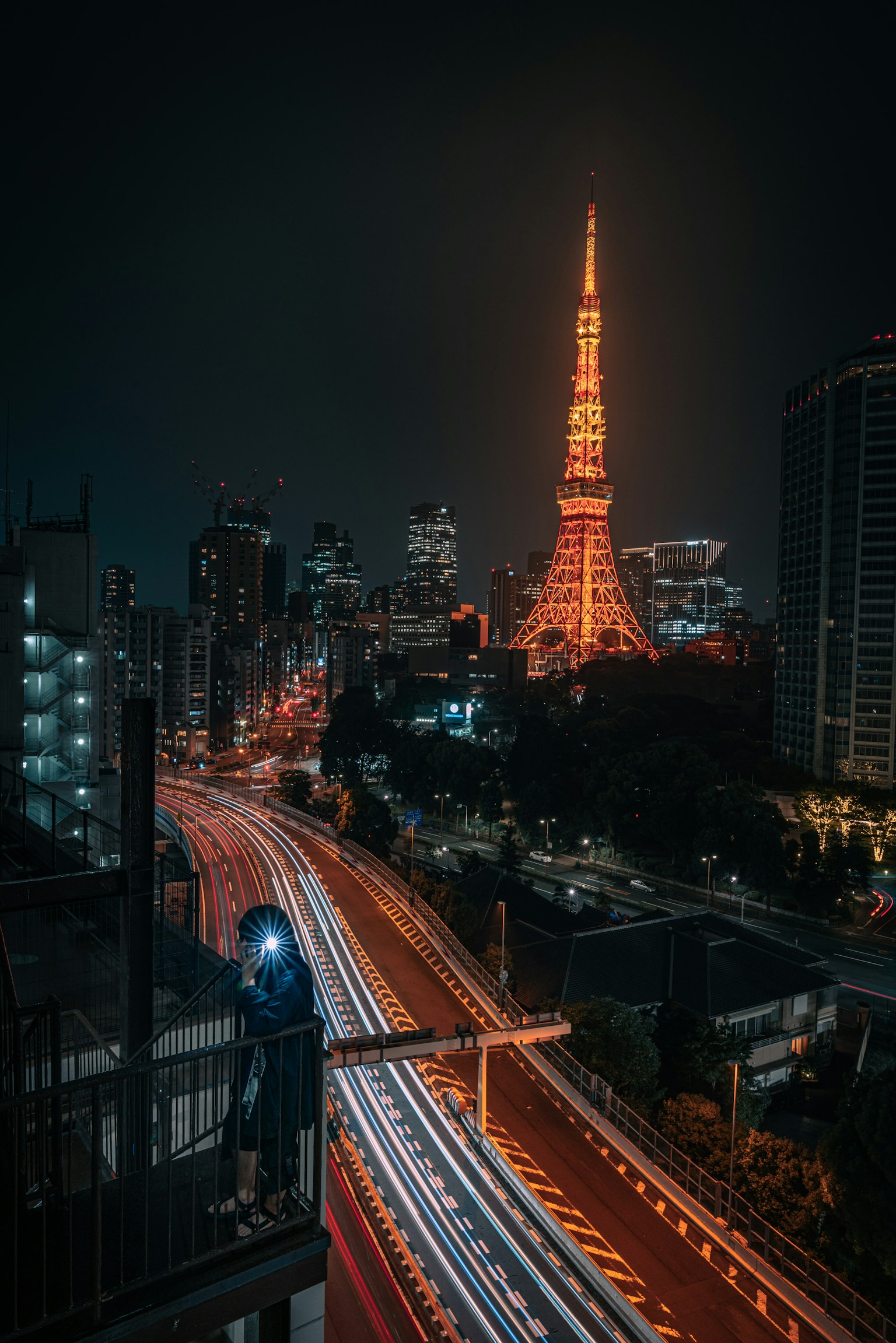 Tokyo Tower illuminated at night with light trails from passing vehicles