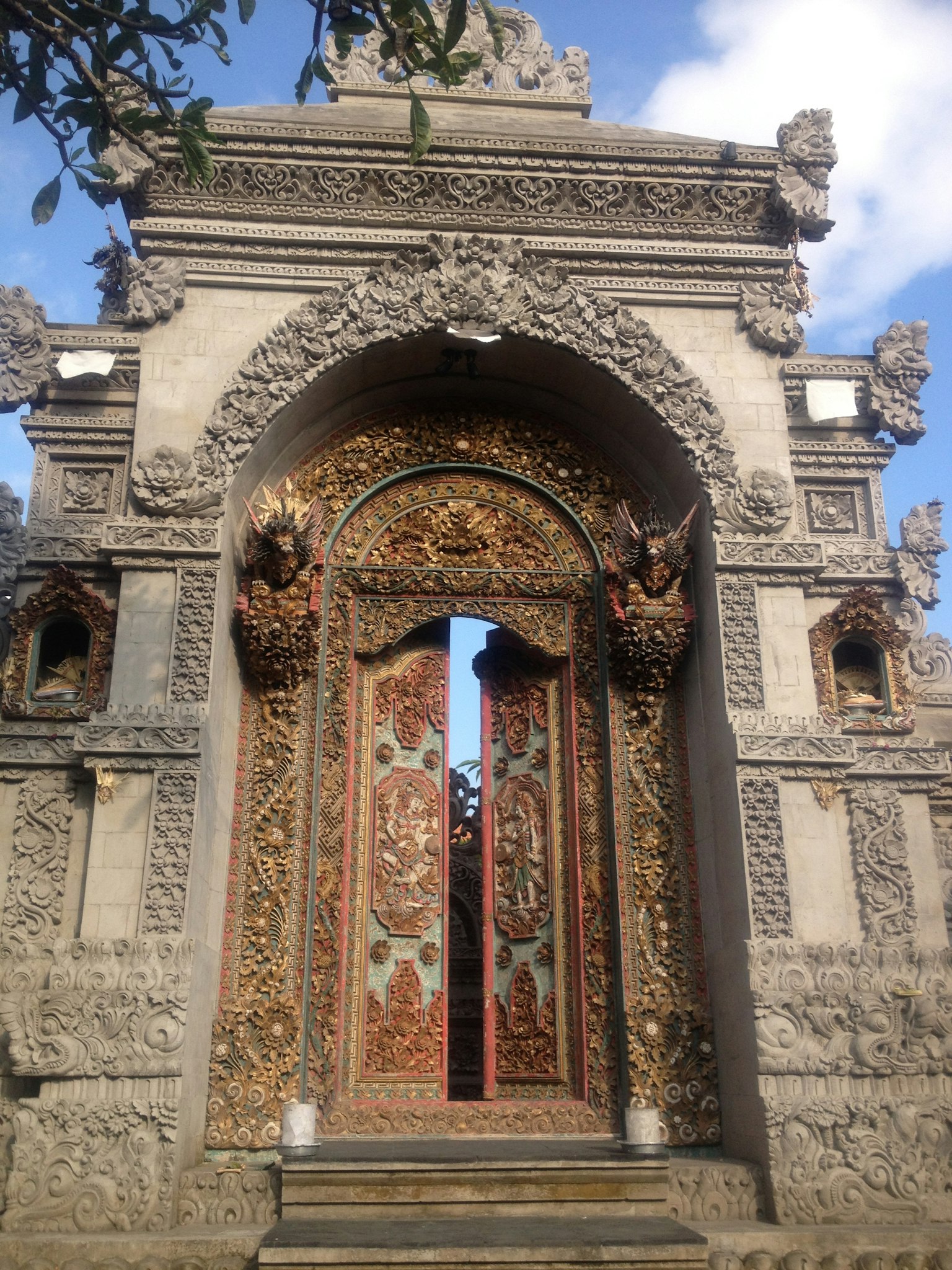 Puerta de templo balinés intrincadamente tallada con colores vibrantes y cielo azul