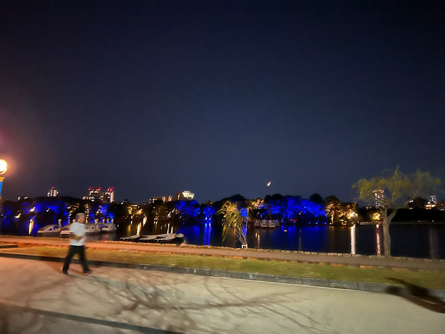 夜の川沿いの風景に青いライトが輝く街並みと人が歩いている