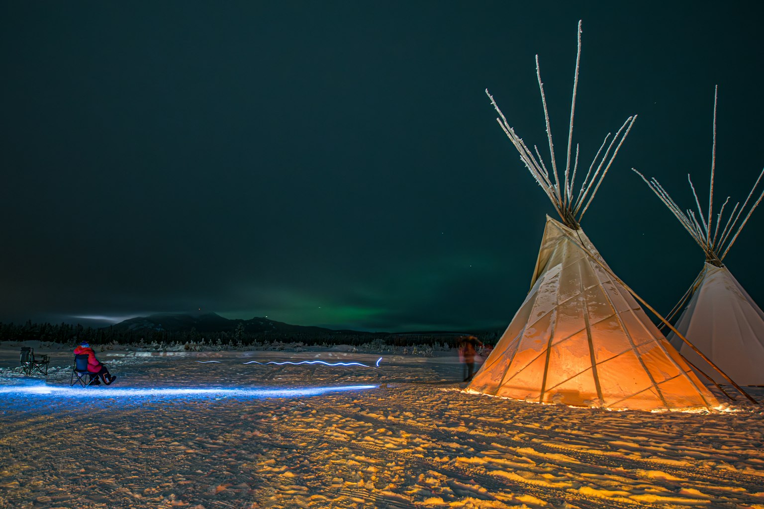Tentes teepee illuminées sur un paysage enneigé sous un ciel d'aurore