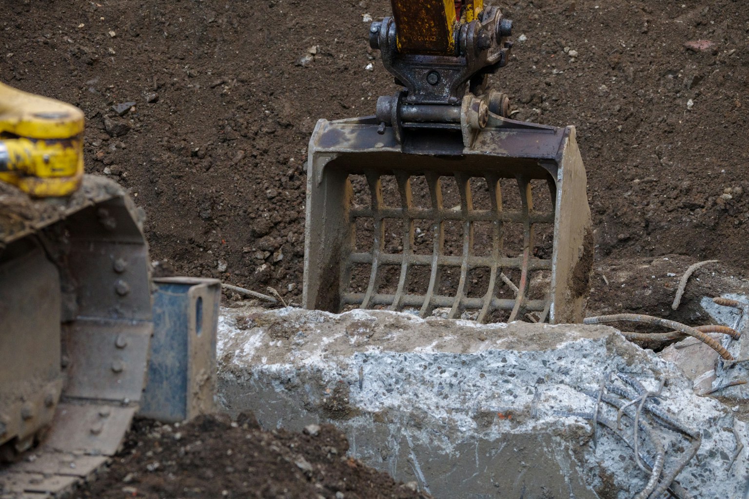 Benna dell'escavatore che scava nel terreno esponendo un tubo di cemento