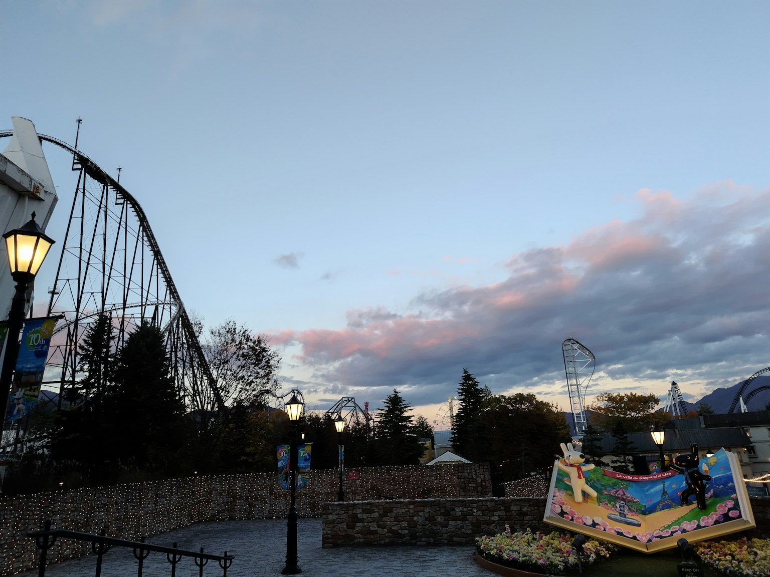 Parc d'attractions au crépuscule avec un grand huit en arrière-plan et un lampadaire et un panneau