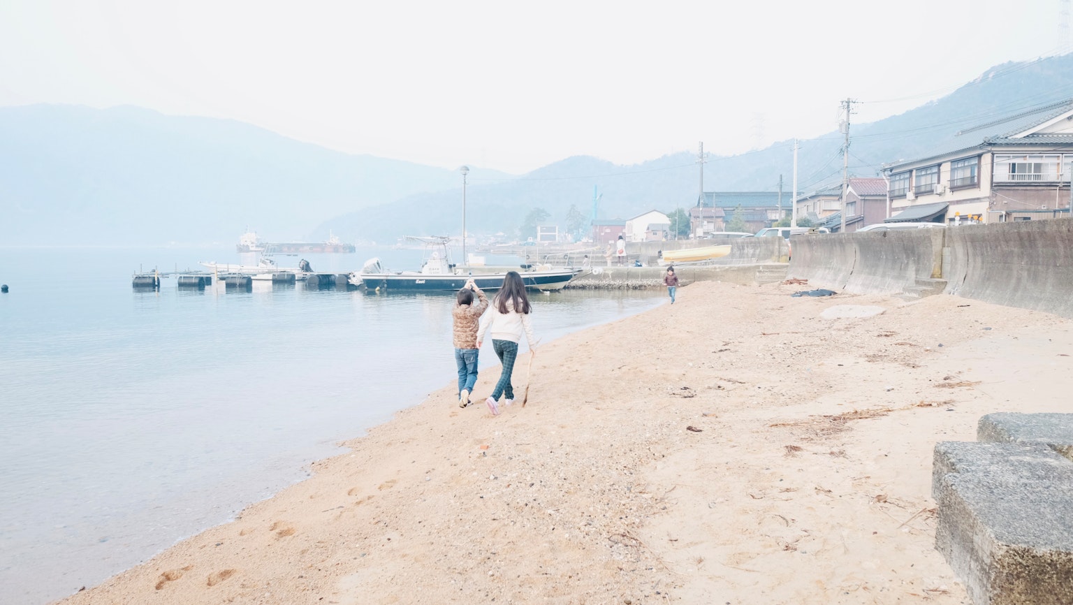 Dos mujeres caminando por una playa con montañas brumosas al fondo