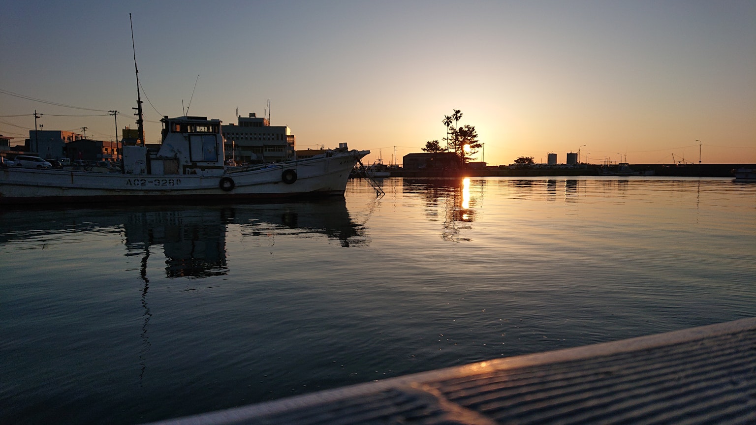 Serene harbor scene with boats silhouetted against a sunset and calm waters