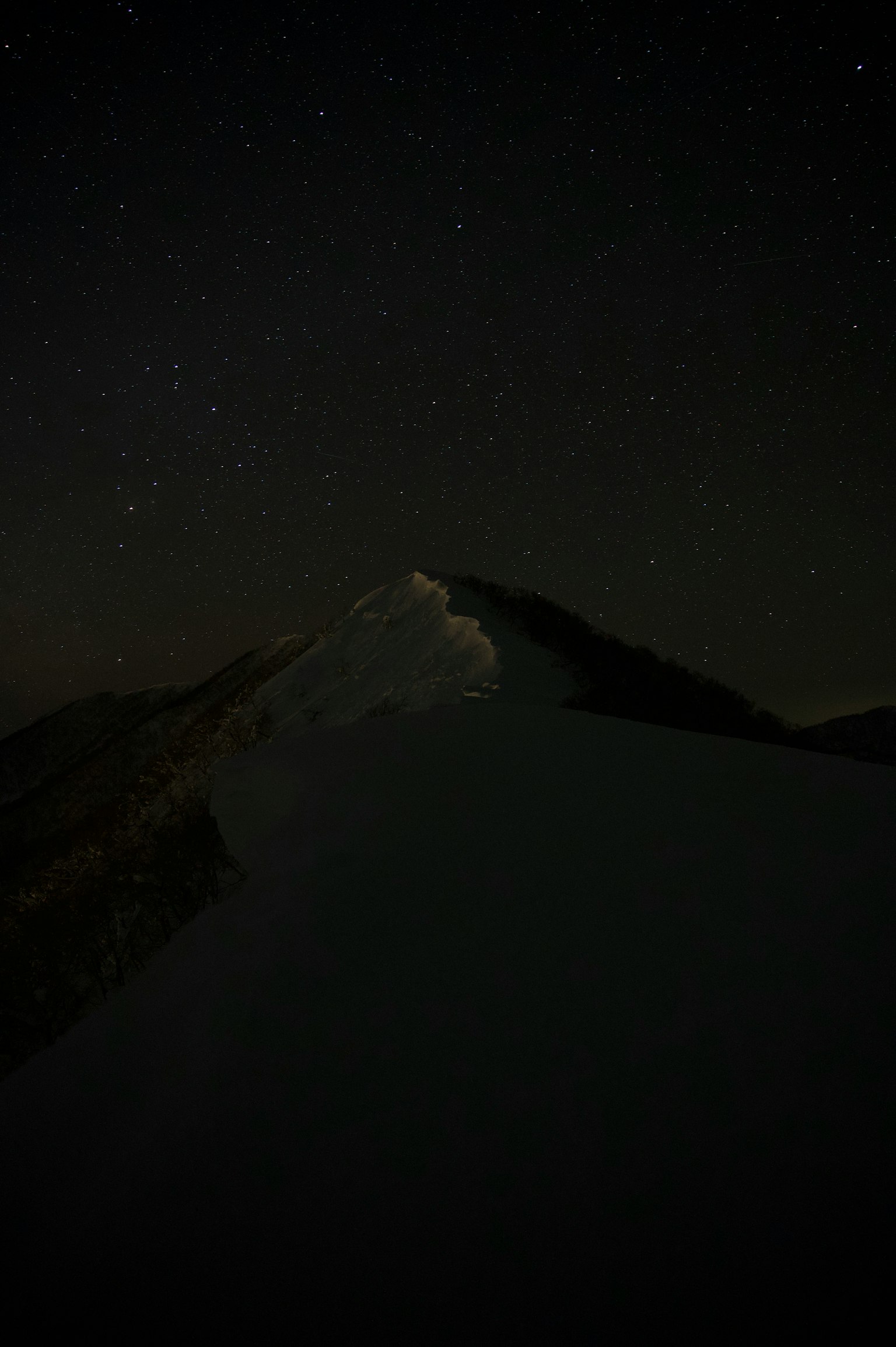 Silhouette of a snow-covered mountain under a starry sky