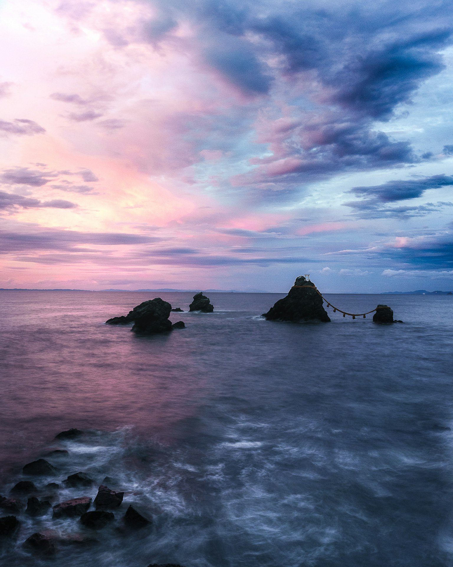 Seascape featuring rocks and a sunset sky