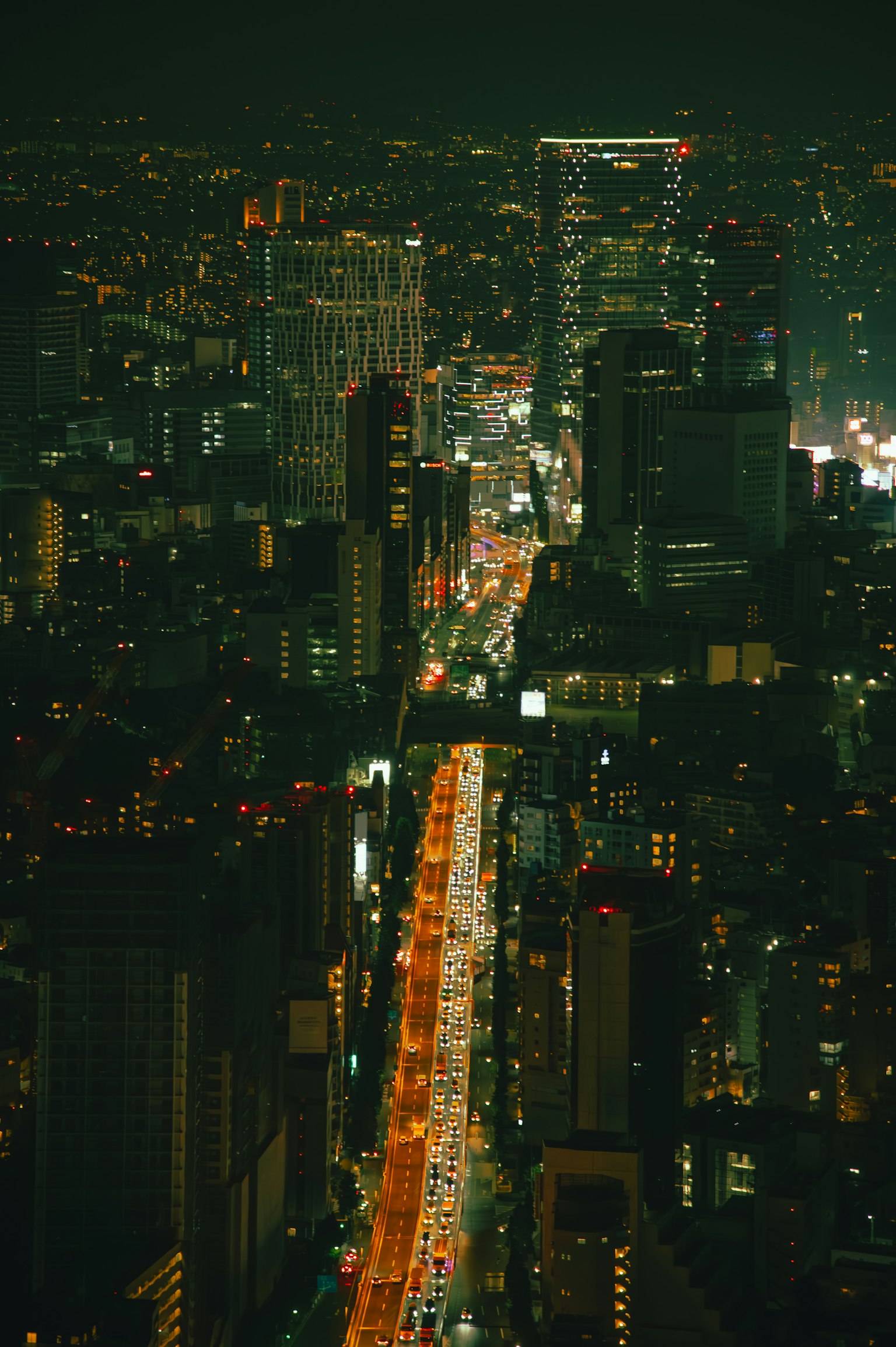 Aerial view of a city at night with a bright road in the center surrounded by numerous buildings