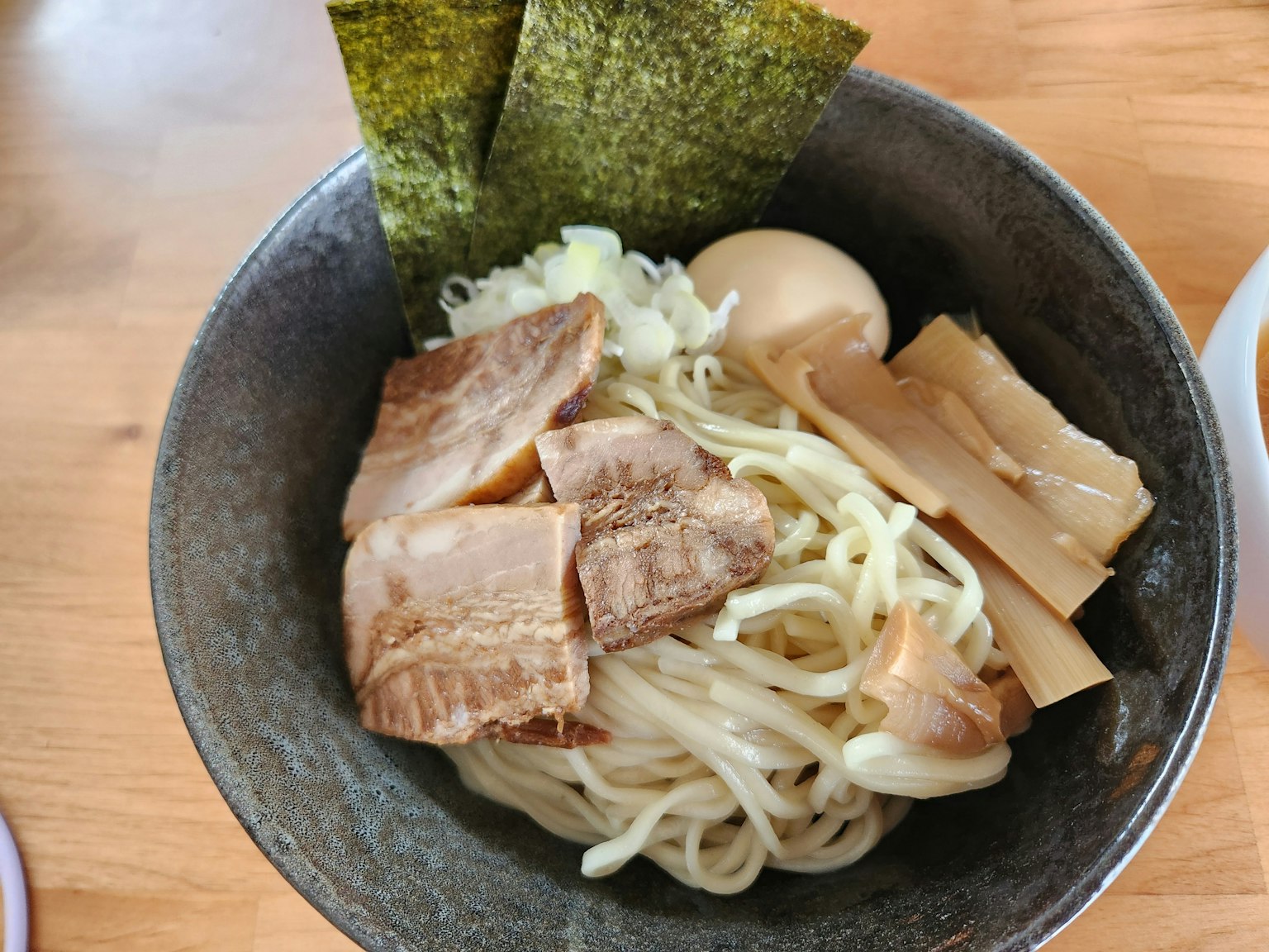 Bowl of ramen with thick noodles topped with slices of chashu pork, soft-boiled egg, menma, and nori