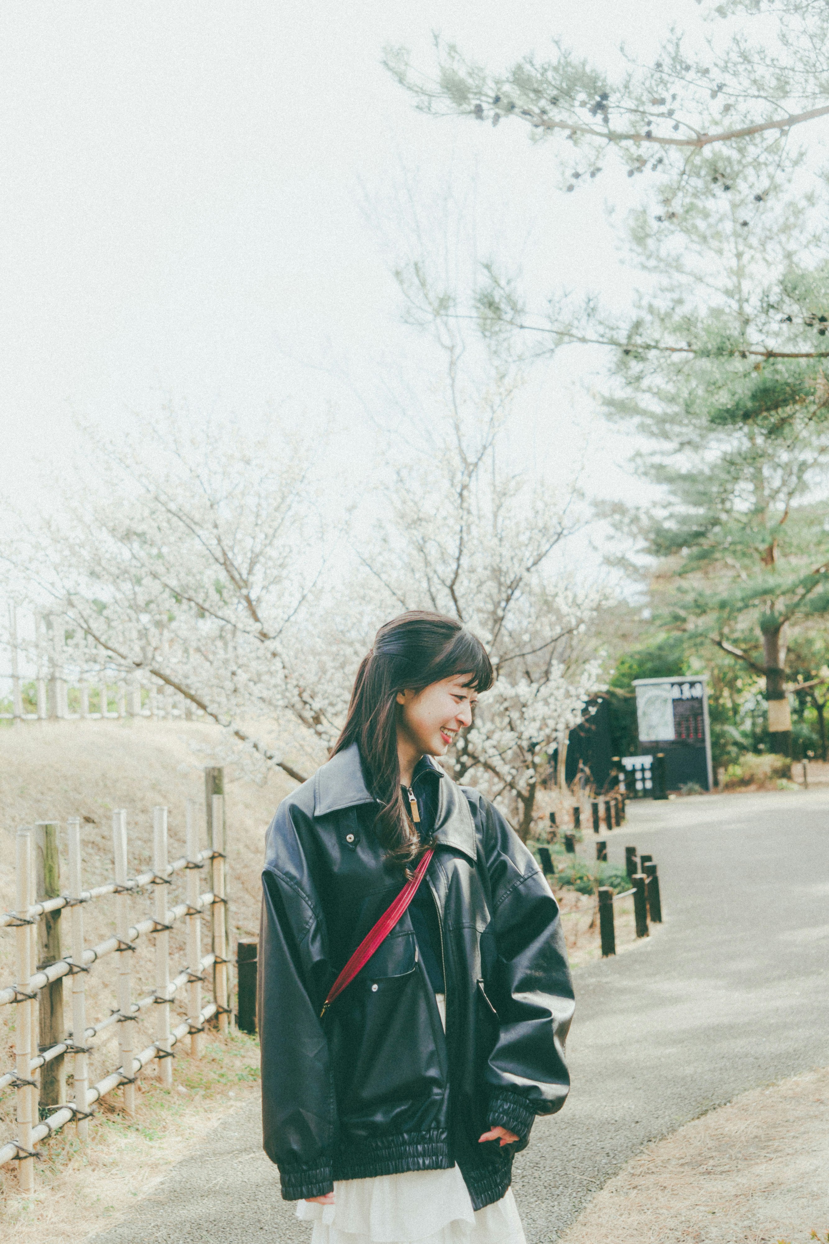 woman in a rain jacket walking along a cherry blossom path
