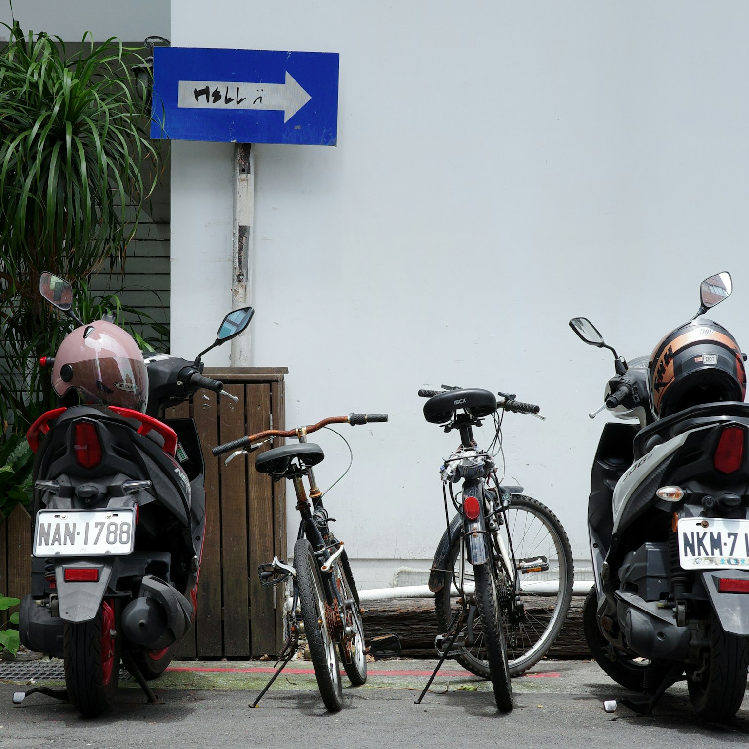 Moto e biciclette parcheggiate affiancate con un cartello direzionale blu sullo sfondo
