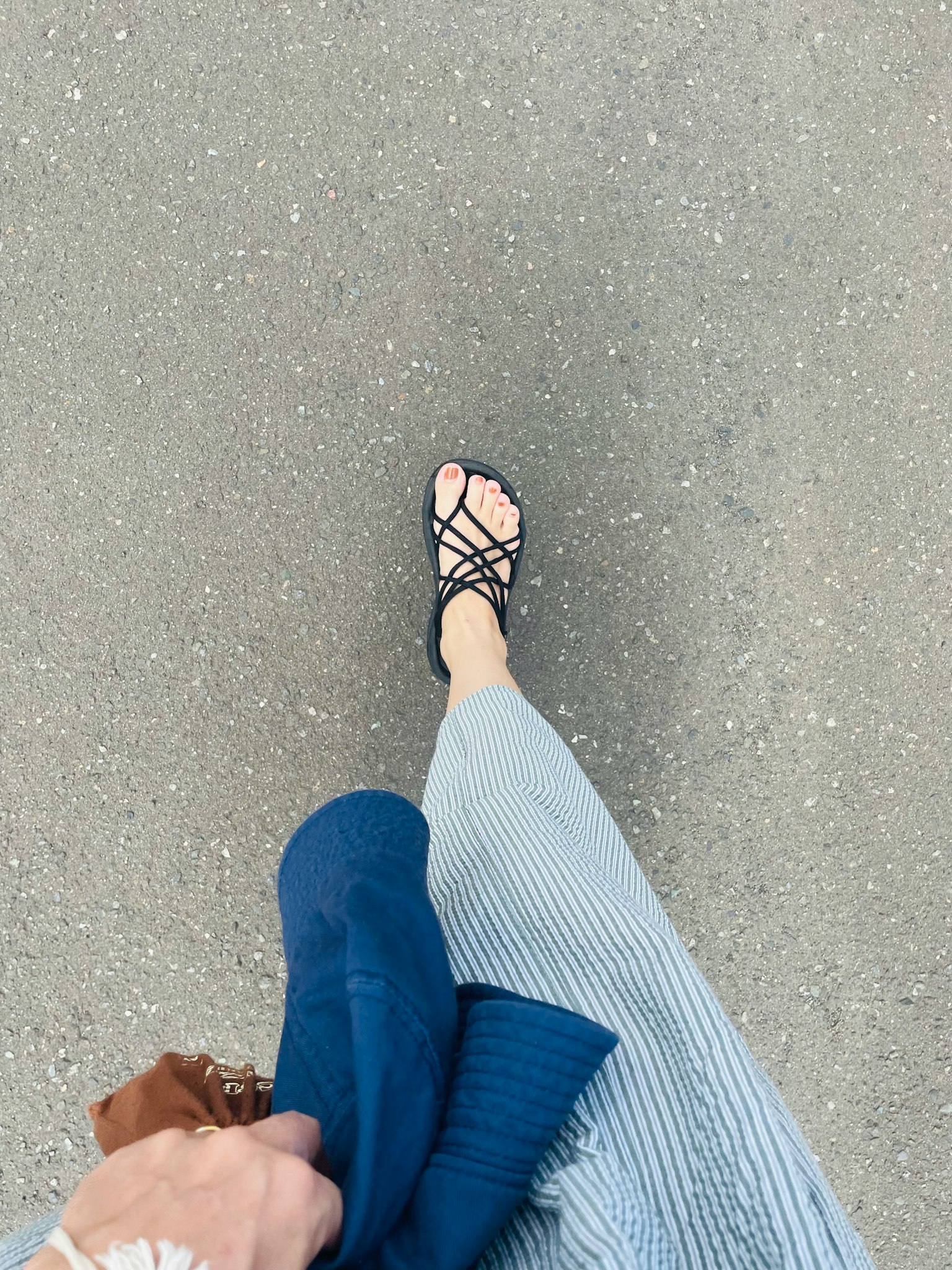 Fuß in schwarzen Sandalen mit gestreiftem Rock und einem blauen Pullover in der Hand