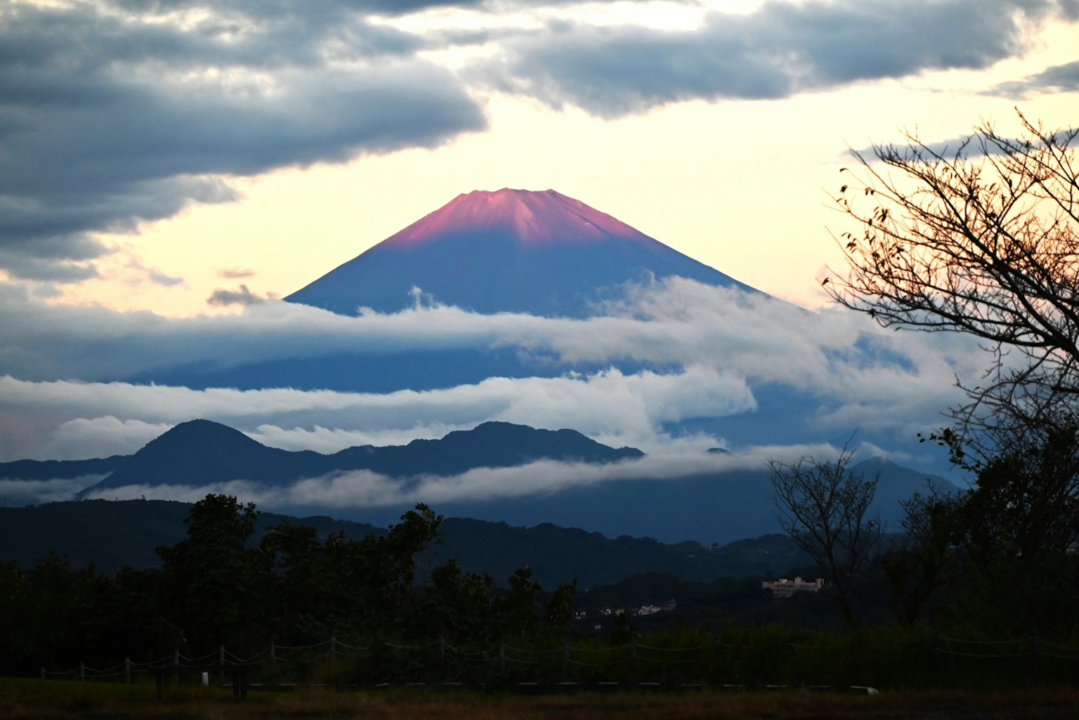 ภูเขาฟูจิที่ถูกแสงอาทิตย์ยามเย็นส่องสว่างพร้อมกับเมฆและเนินเขาไกลๆ