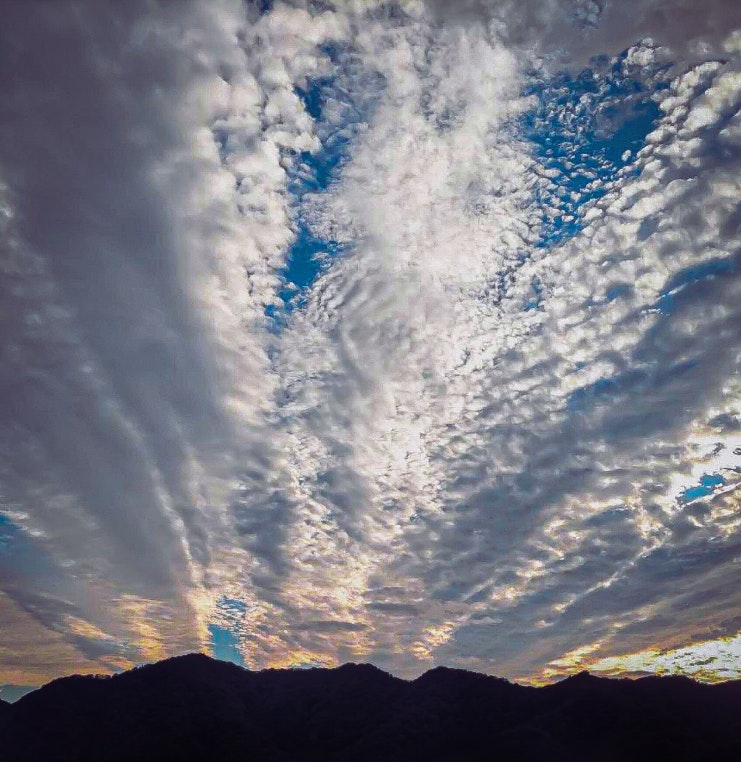 放射状のうろこ雲が広がる夕焼けの空と山並みのシルエット