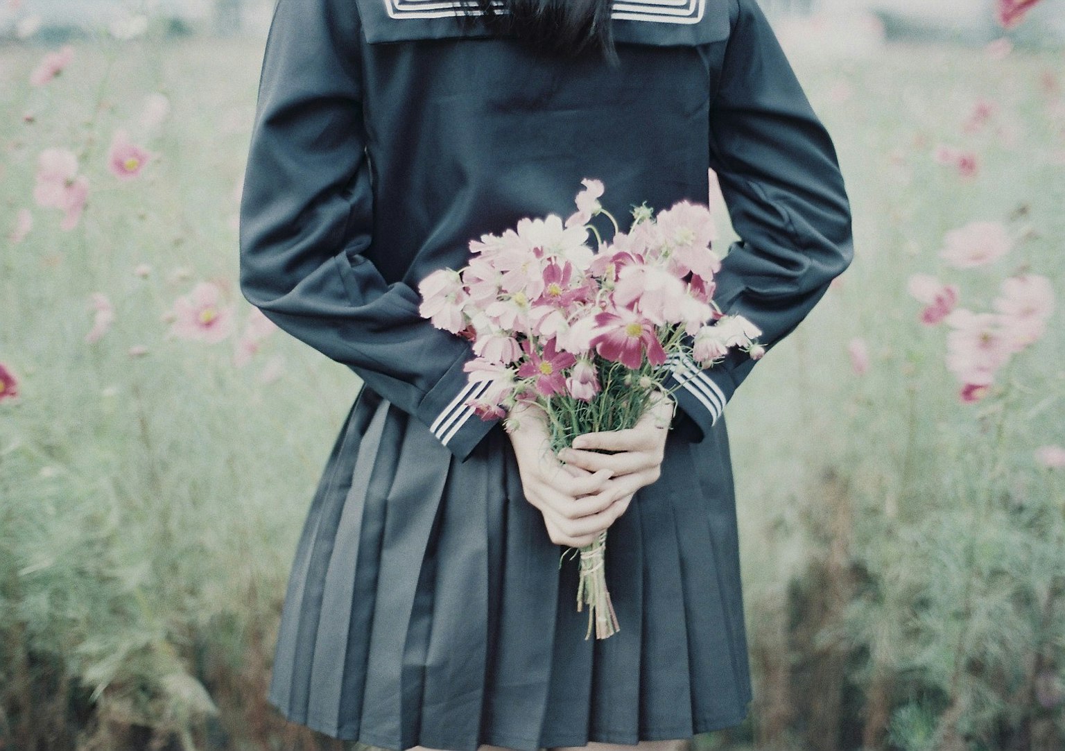 Girl holding a bouquet in a blue uniform standing in a flower field