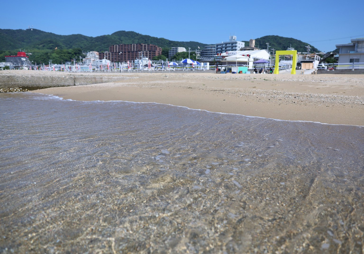 Vista di acqua trasparente e spiaggia di sabbia con montagne e edifici sullo sfondo