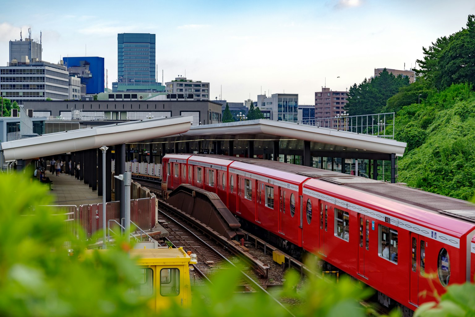 Kereta merah di stasiun dengan bangunan kota dan taman di latar belakang