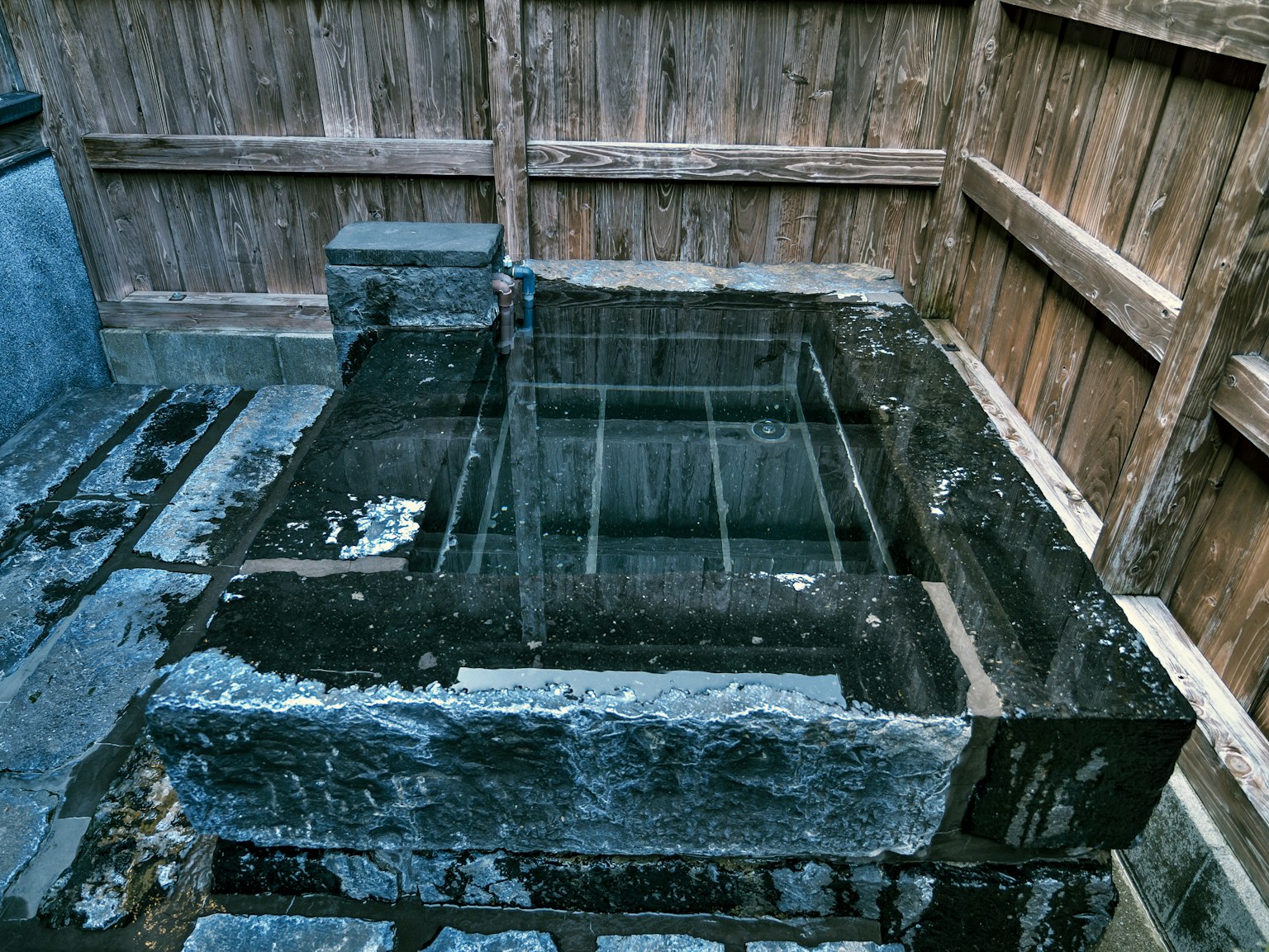 Bacino d'acqua in pietra circondato da una recinzione in legno in un giardino tranquillo