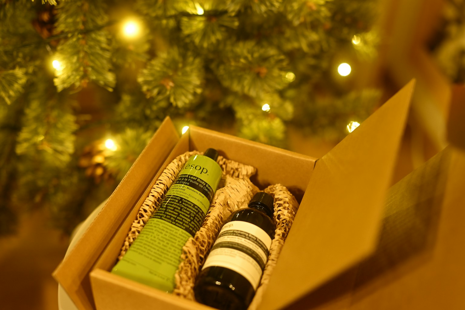 Open box with green towels and a bottle in front of a Christmas tree