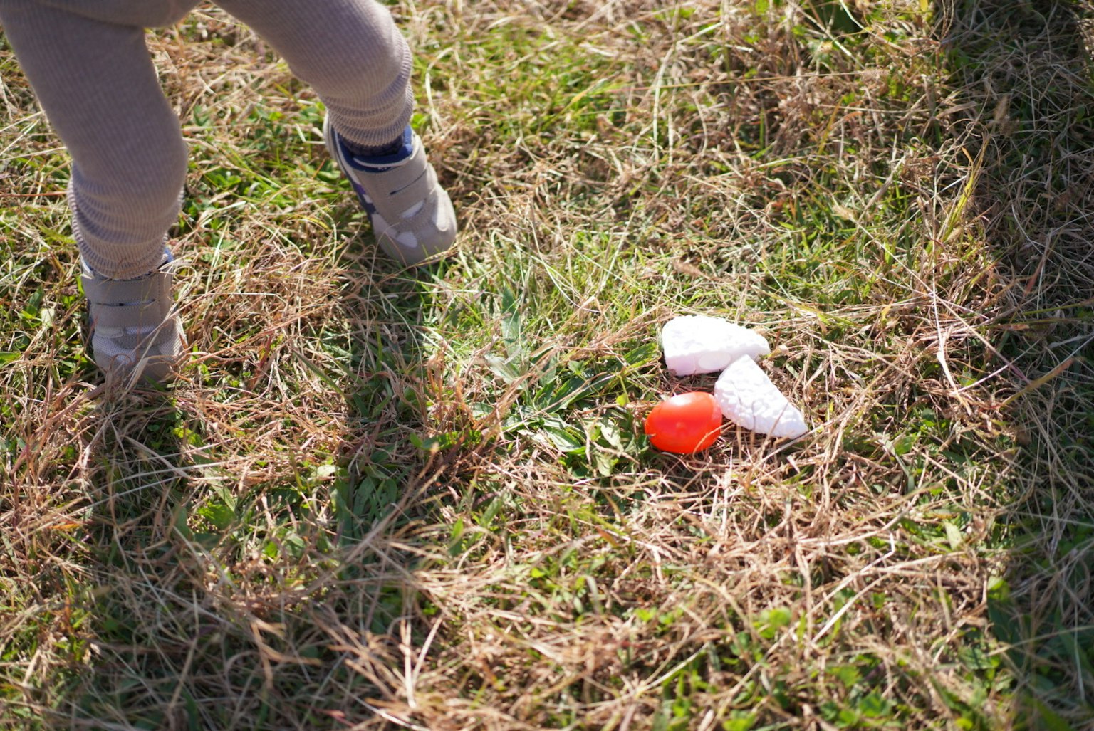 Piedi di bambino vicino a oggetti colorati a forma di uovo sull'erba