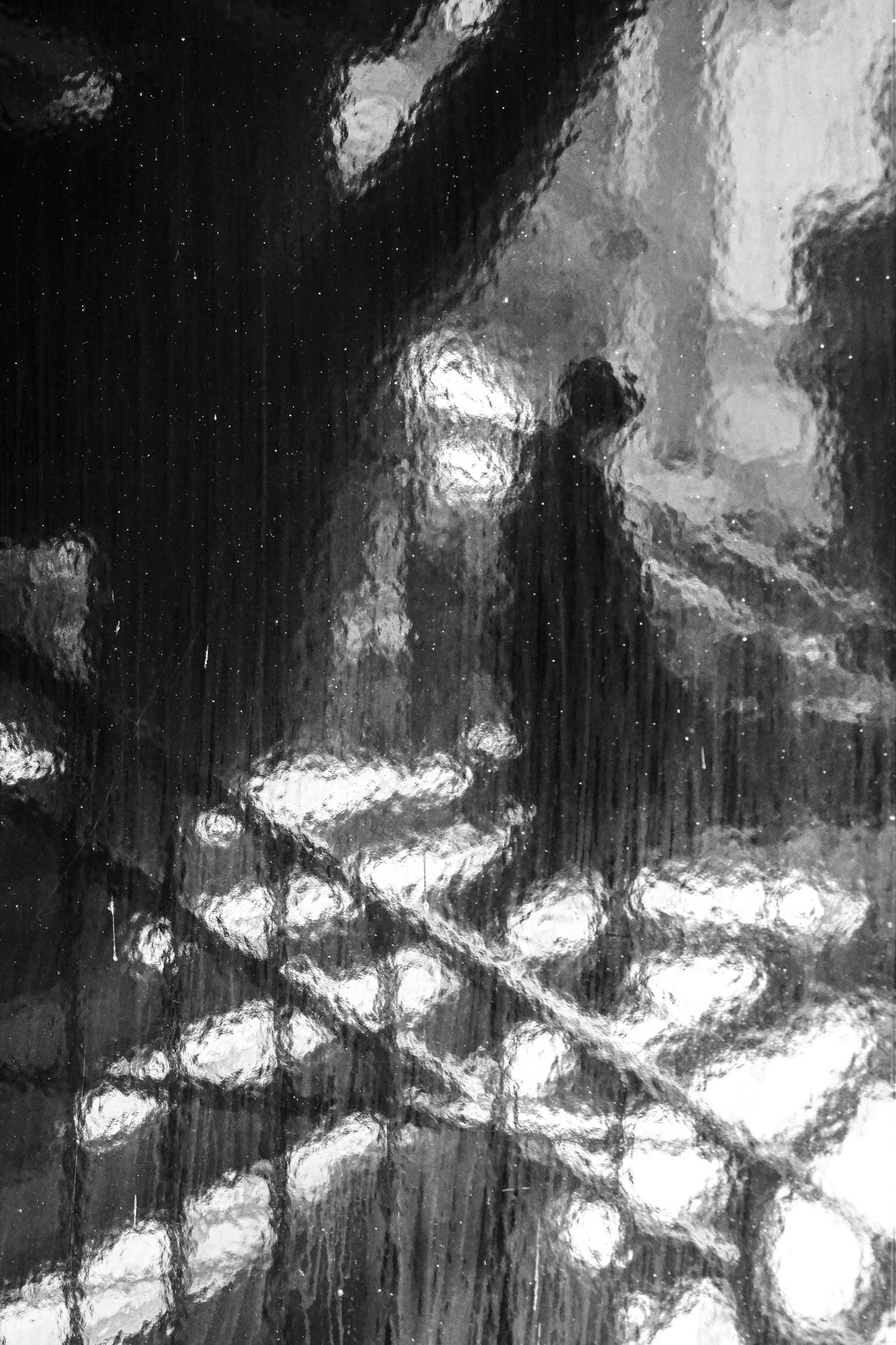 雨粒の付いた窓ガラス越しの街灯と人影