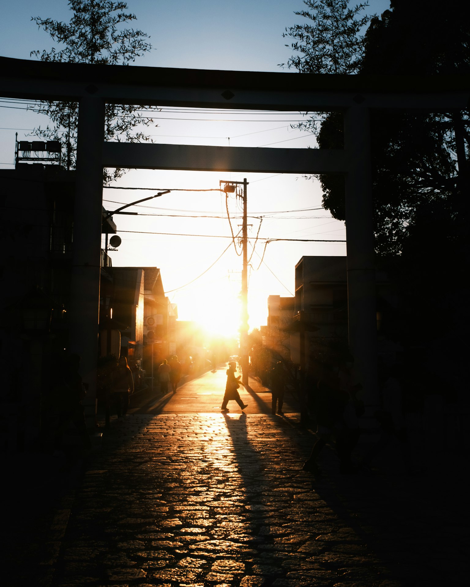 Silhouette di una persona che cammina attraverso un torii al tramonto