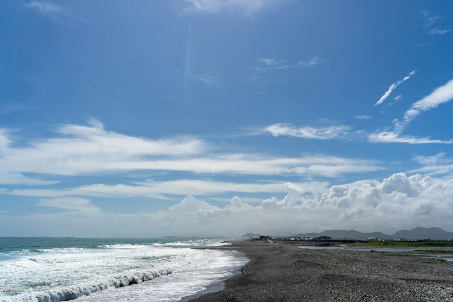 Paesaggio di spiaggia con cielo blu e nuvole bianche onde che si infrangono sulla sabbia nera
