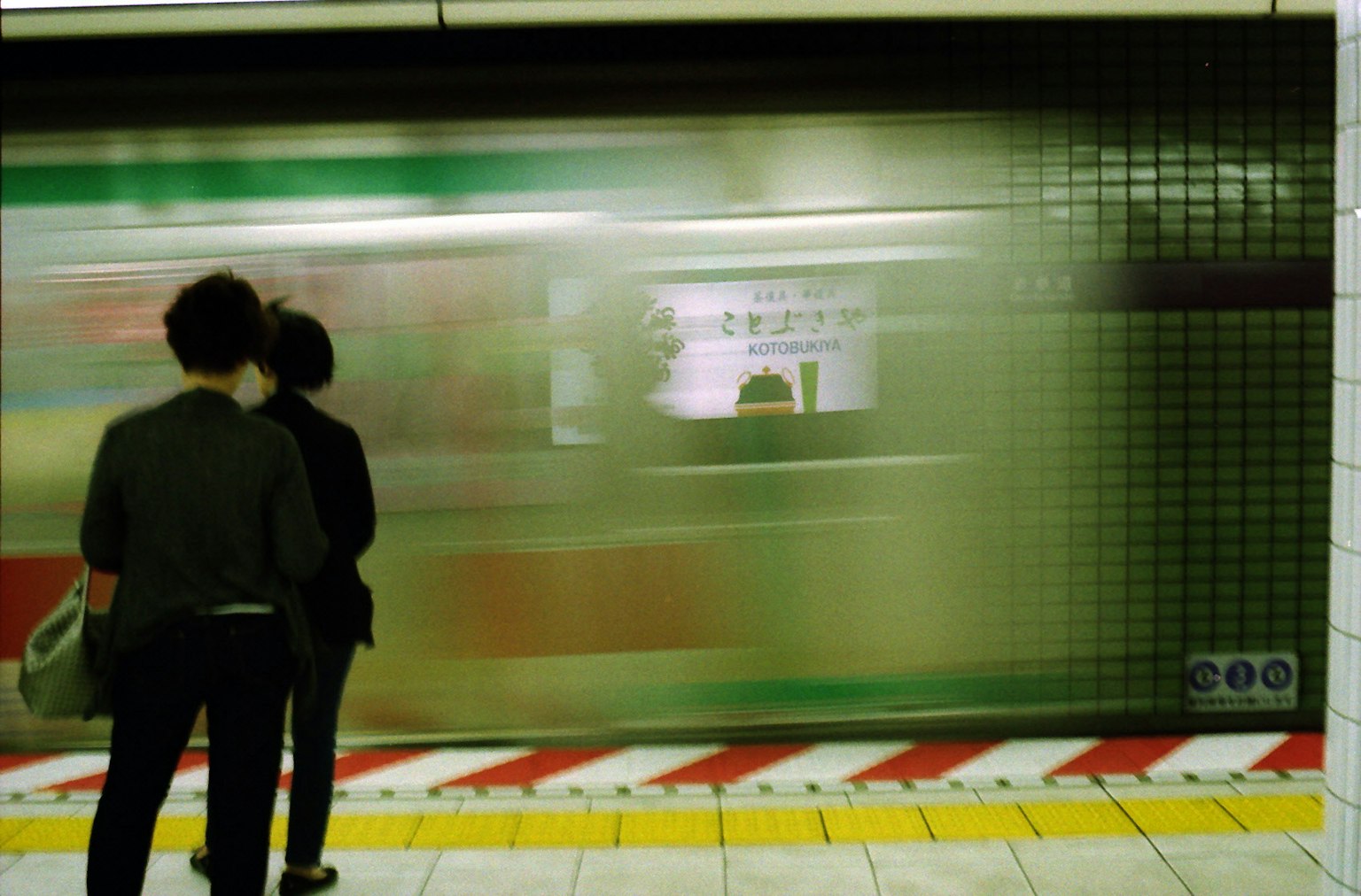 Siluetas de dos personas esperando en una plataforma de metro con un tren que pasa