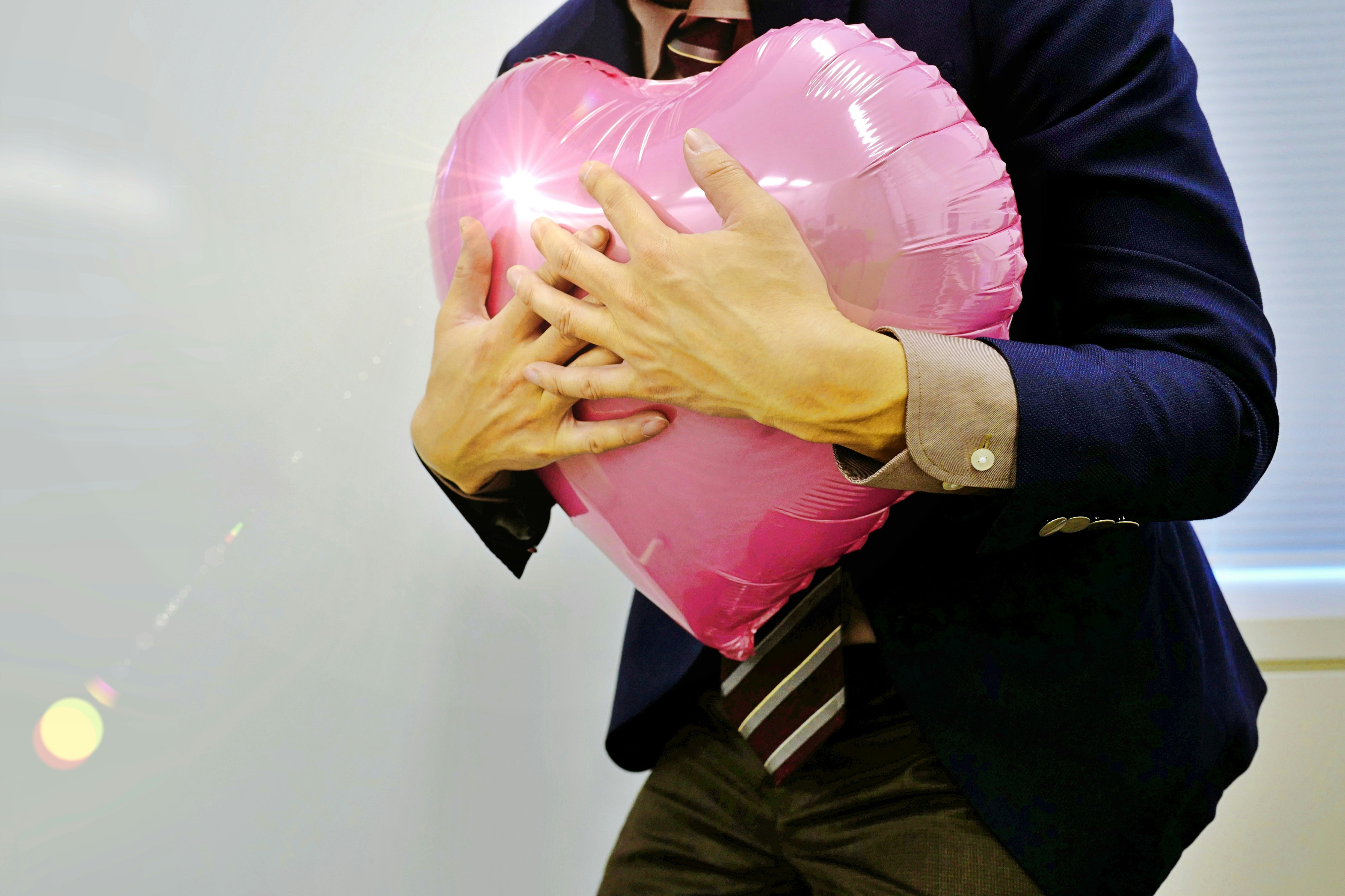 Valentine embrace with hands holding a pink heart balloon
