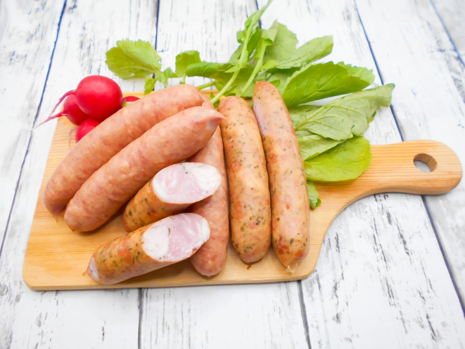 Salsicce su un tagliere di legno con ravanelli freschi e verdure a foglia