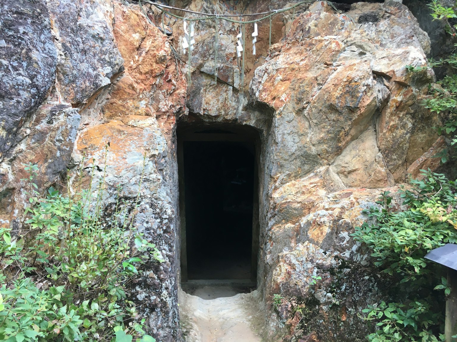 Entrata di una caverna buia circondata da formazioni rocciose e vegetazione lussureggiante