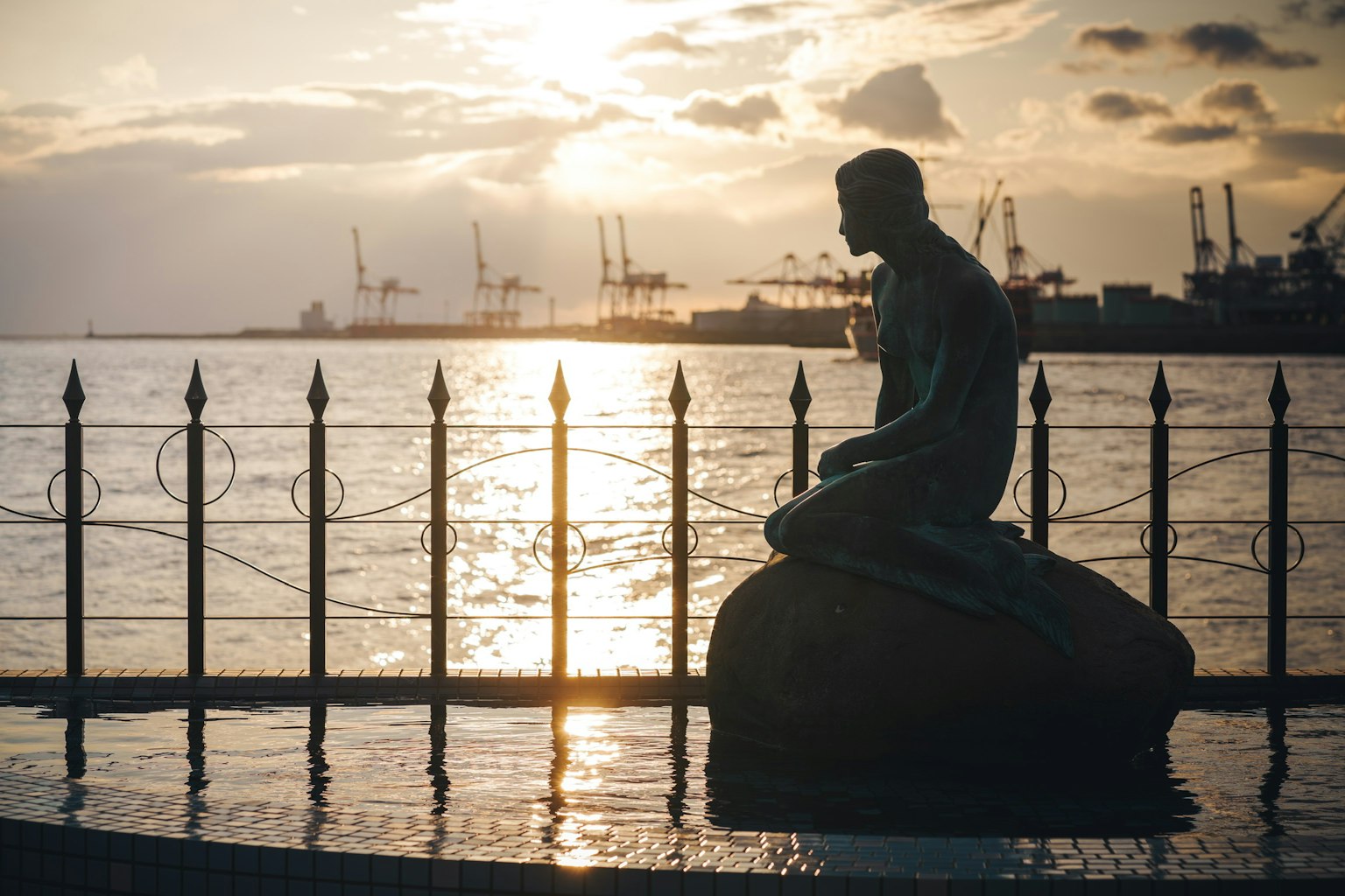 Statue de sirène assise au bord du port au coucher du soleil