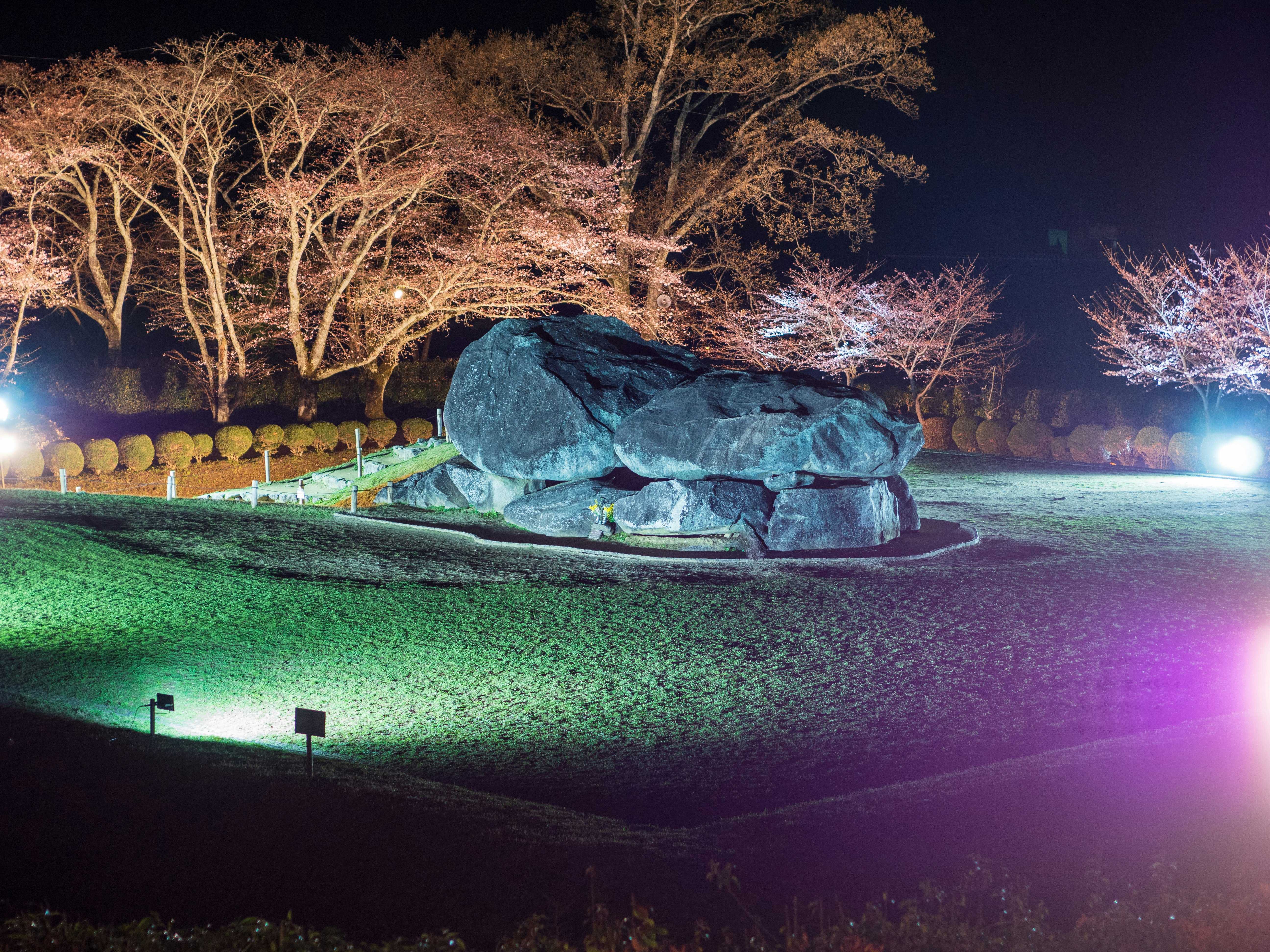 nighttime park scene with a large illuminated stone sculpture and lawn