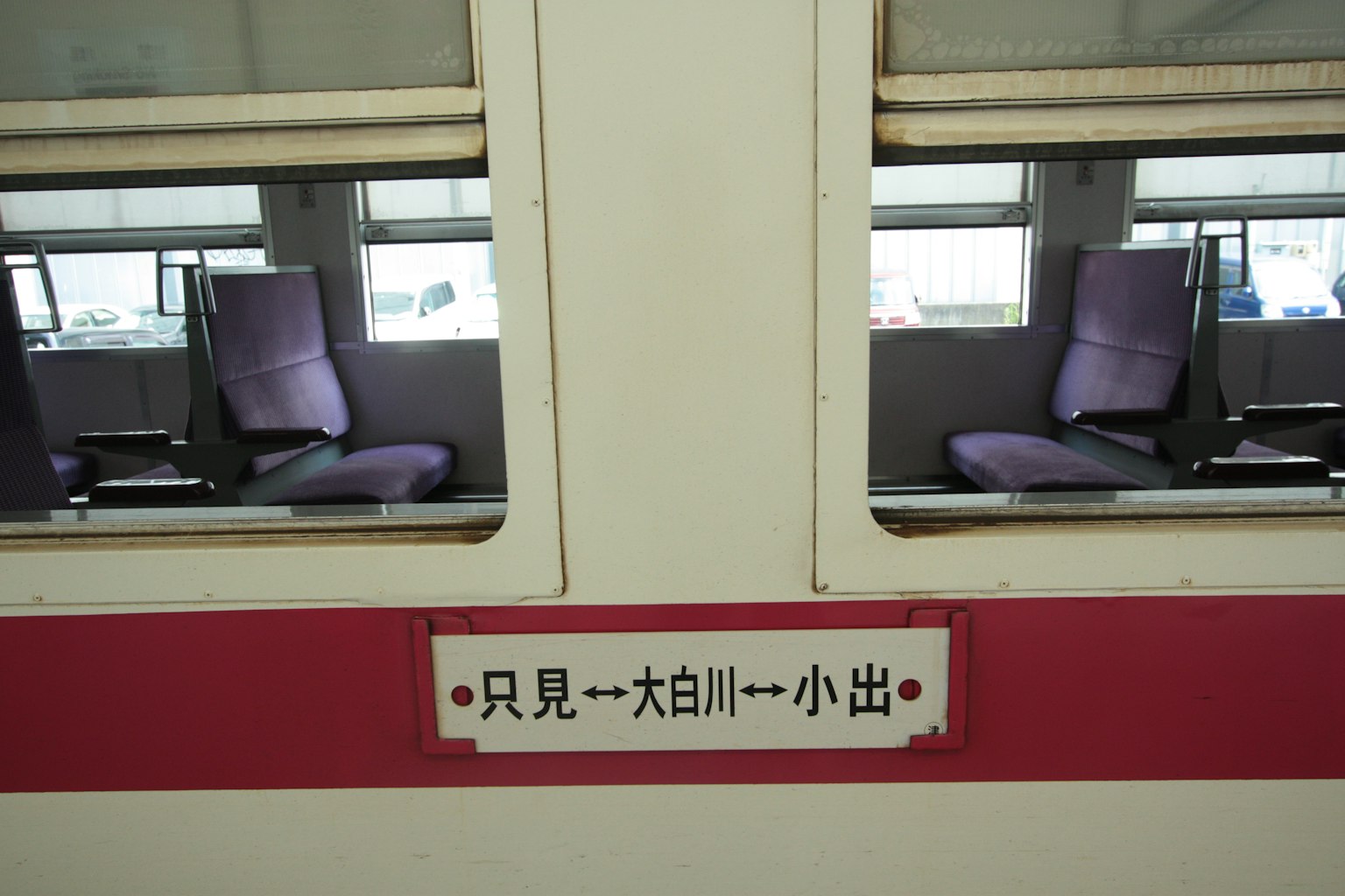 Pemandangan interior kereta dengan kursi ungu dan tanda stasiun