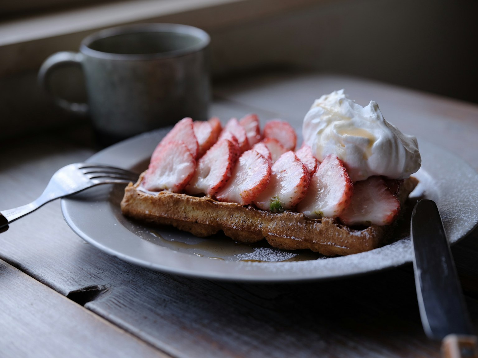 Teller mit Waffeln, belegt mit frischen Erdbeeren und Schlagsahne, neben einer Kaffeetasse