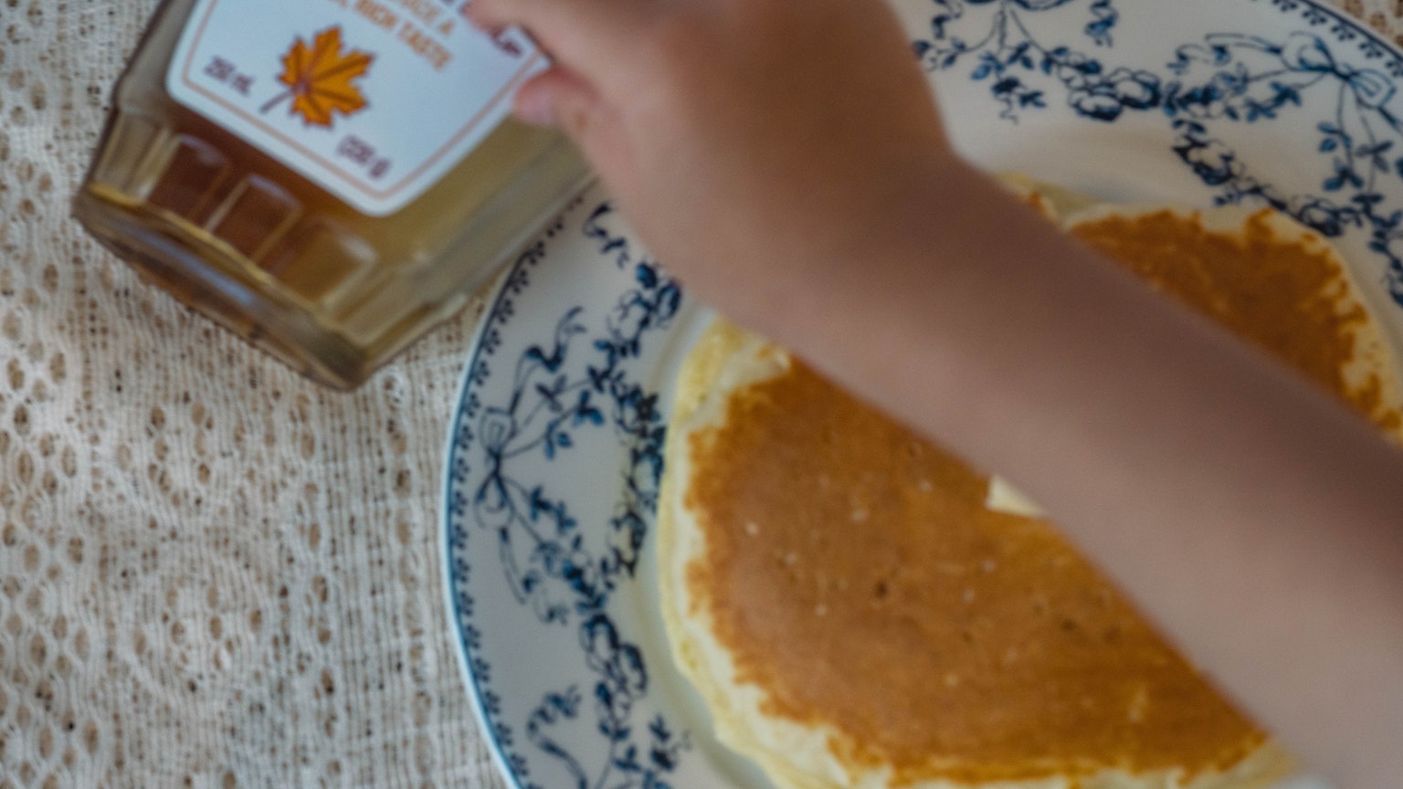 Sebuah tangan menuangkan sirup maple di atas pancake di piring dekoratif