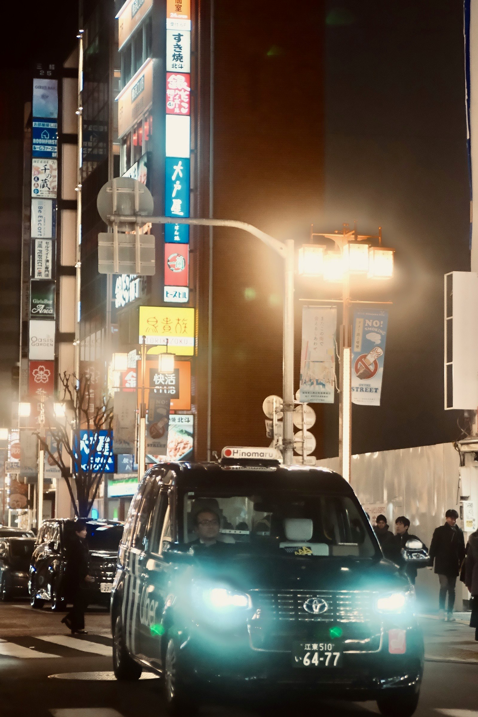 夜の街並みを走るクラシックカーと人々の往来