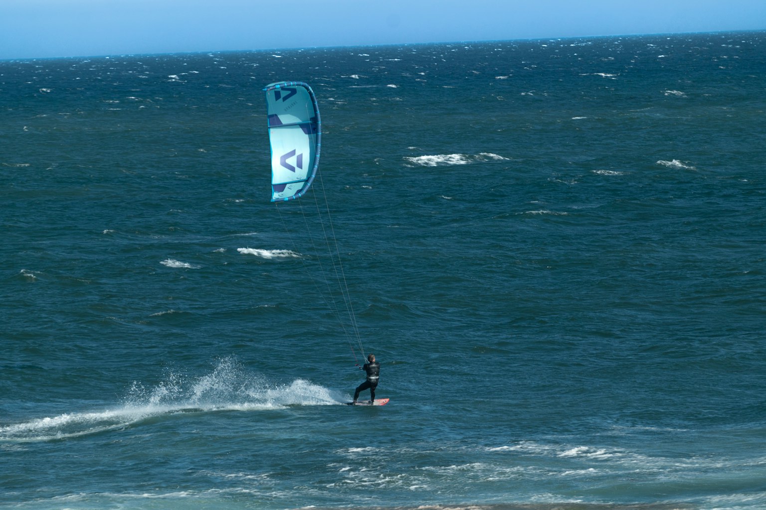 Person kitesurfing on the ocean with a blue kite and waves