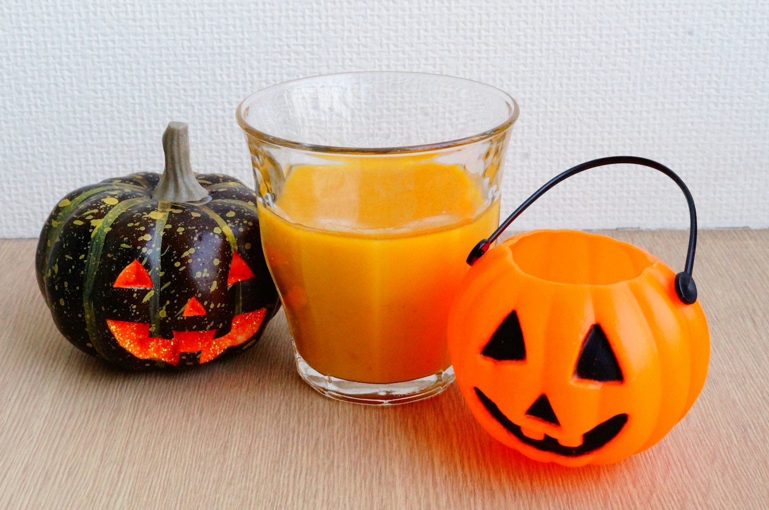 Una configuración temática de Halloween con una calabaza tallada, un vaso de jugo de naranja y un recipiente en forma de calabaza naranja
